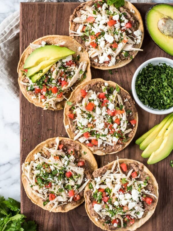 These crispy and crunch Slow Cooker Salsa Verde Chicken Tostadas are topped with a layer of delicious refried beans, salsa verde chicken, tomatoes, cilantro queso fresco and avocados.