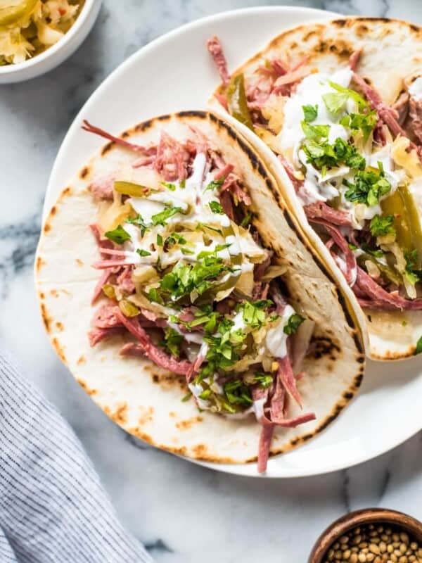 Slow cooker corned beef tacos in a flour tortilla topped with sauerkraut and sour cream.