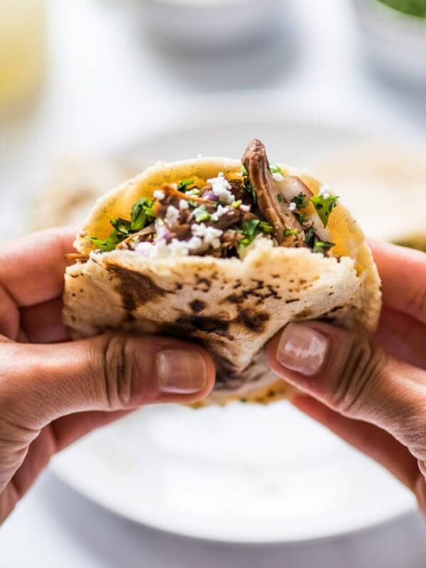 Two hands hold a gordita stuffed with meat and cheese.