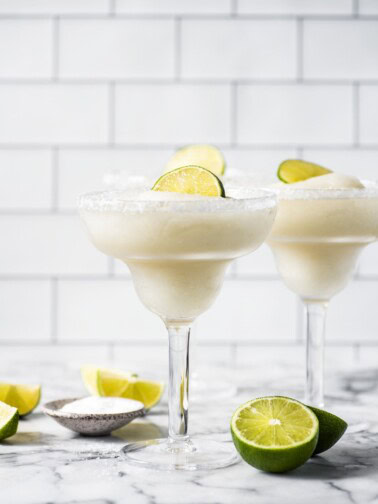 Frozen margaritas in glasses topped with lime wedges.