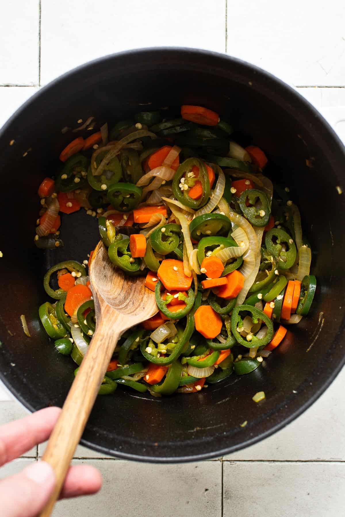 Jalapeño peppers, onions, and carrots satueed in a large pot.