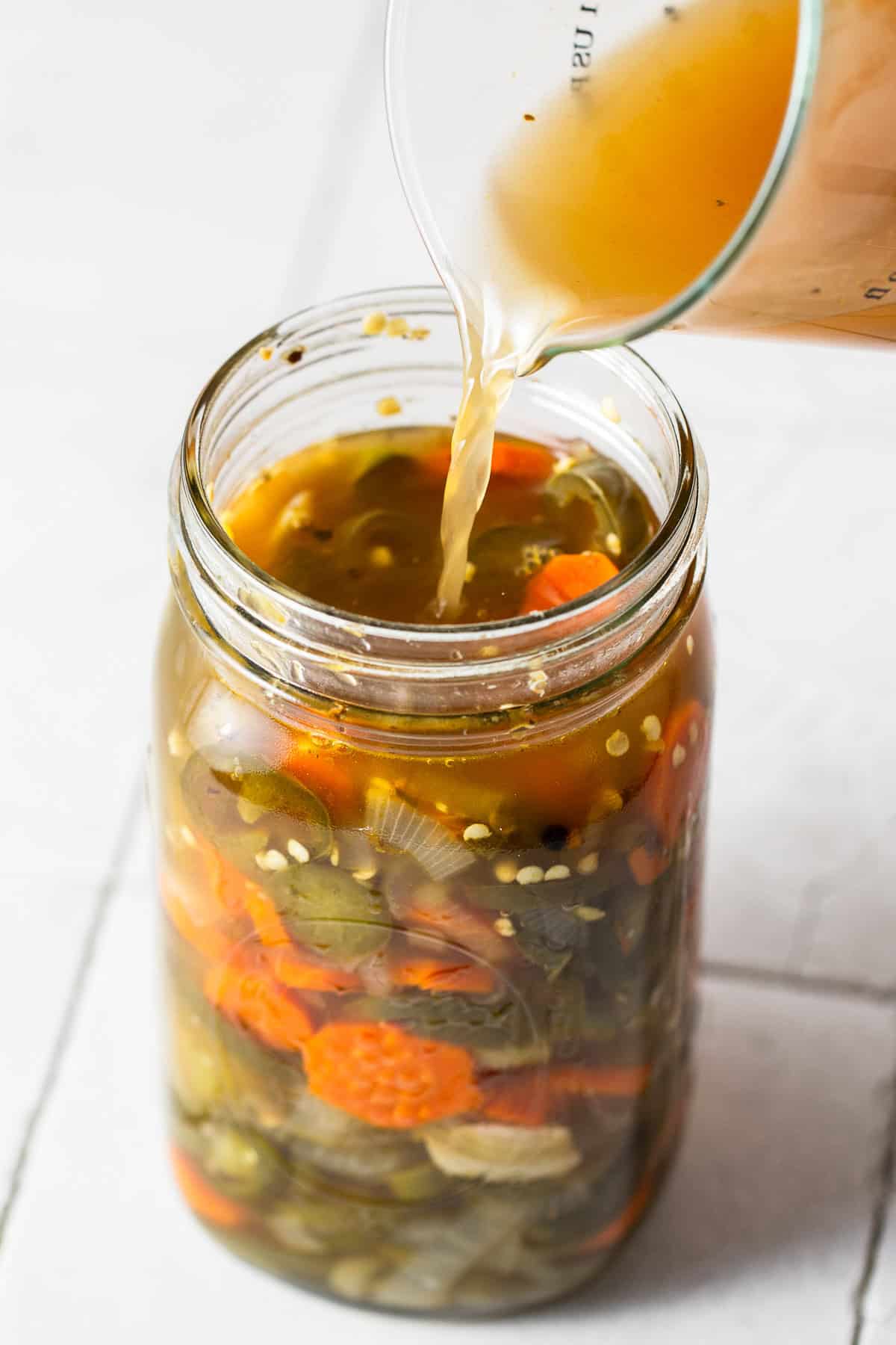 Pickling liquid being poured into a jar of pickled jalapenos.