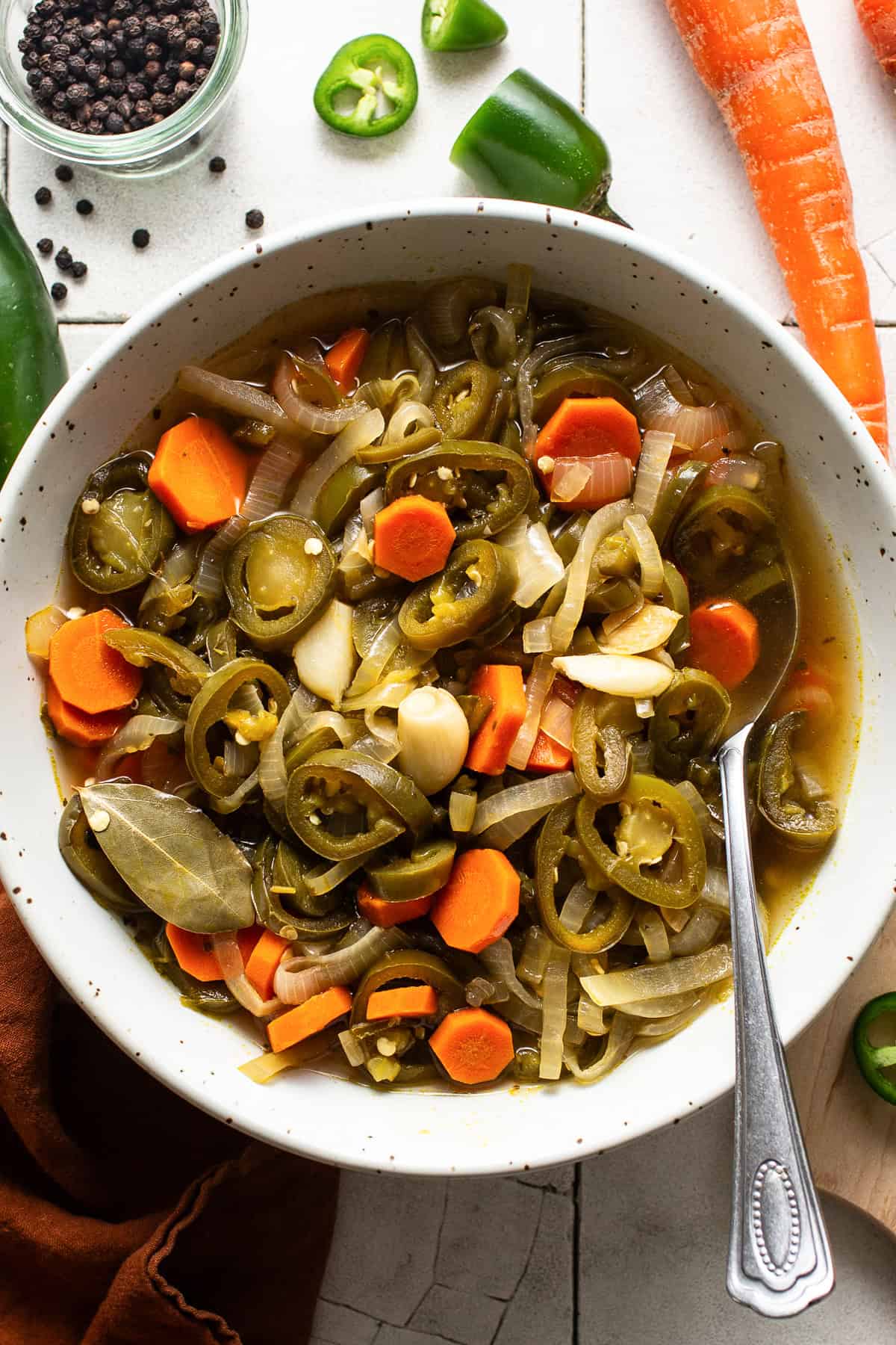 A bowl of pickled jalapeños Mexican escabeche style with carrots, onions, and garlic on a table.