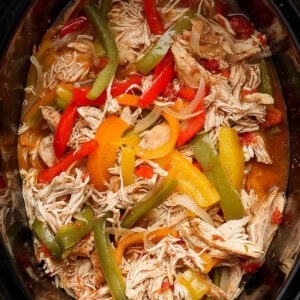 Crockpot chicken fajitas in a slow cooker with bell peppers and onions.