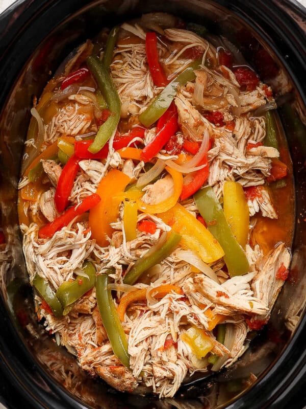 Crockpot chicken fajitas in a slow cooker with bell peppers and onions.