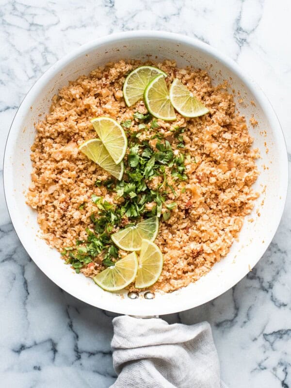 Mexican cauliflower rice in skillet garnished with cilantro and lime.