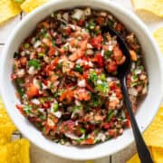 Homemade salsa made from tomatoes, onion, cilantro, jalapeños, and more, in a white bowl surrounded by tortilla chips.