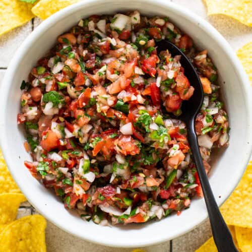 Homemade salsa made from tomatoes, onion, cilantro, jalapeños, and more, in a white bowl surrounded by tortilla chips.