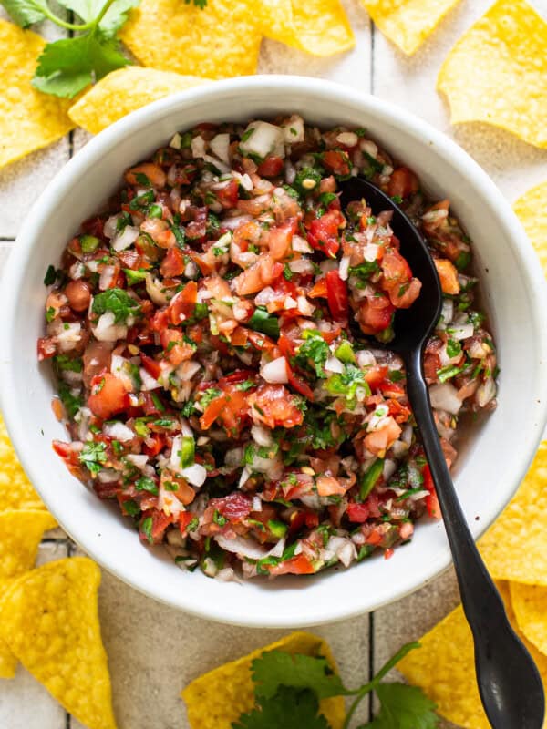 Homemade salsa made from tomatoes, onion, cilantro, jalapeños, and more, in a white bowl surrounded by tortilla chips.