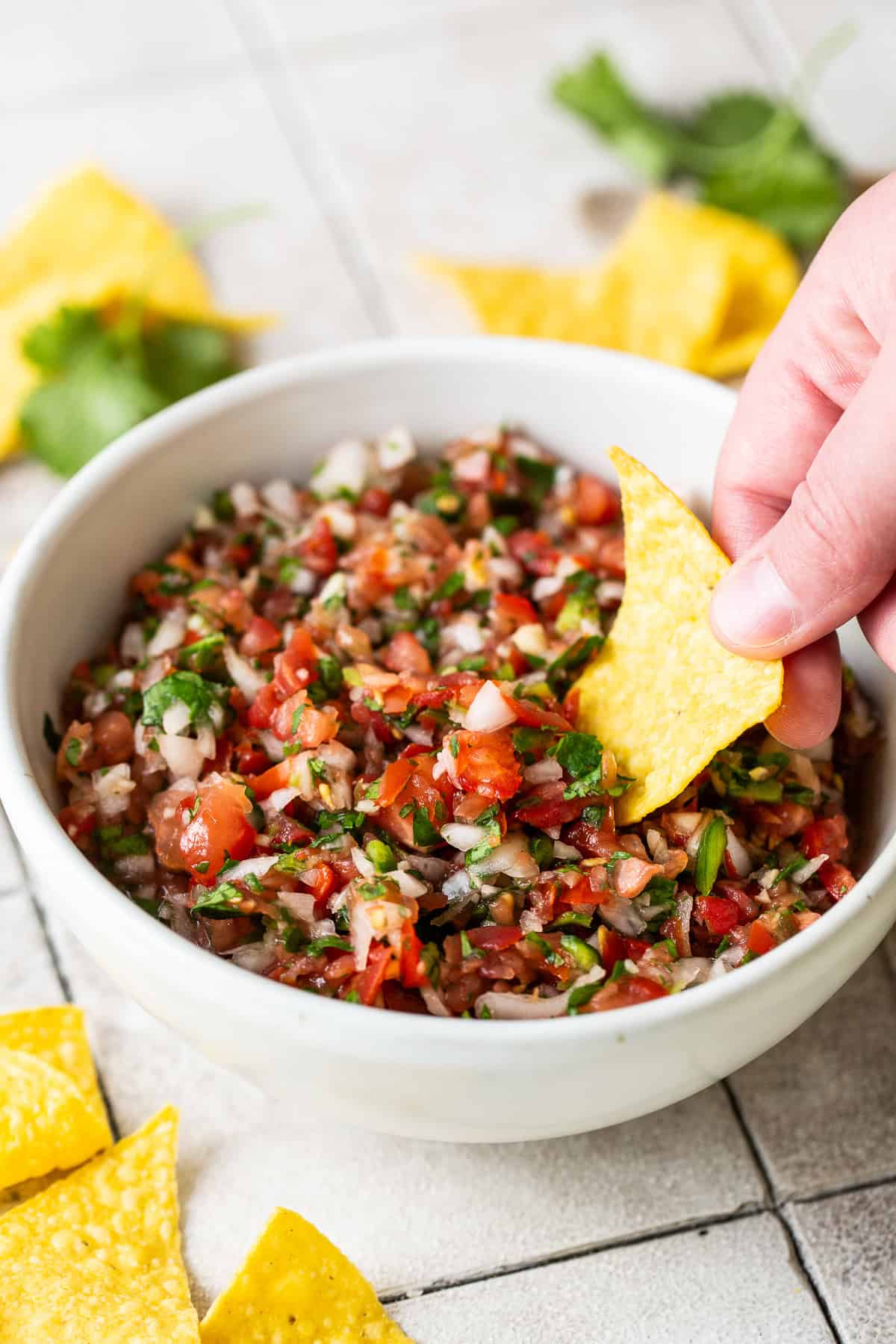 A tortilla chip being dipped into a bowl of homemade salsa.