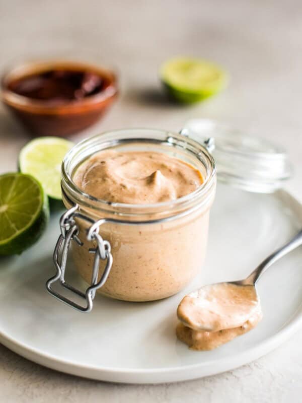 Chipotle sauce recipe in a small glass container surrounded by limes and chipotle peppers.