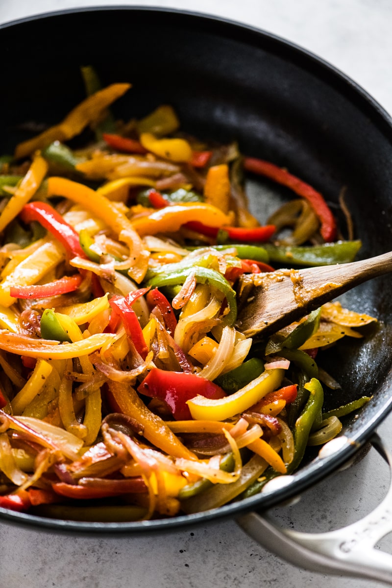 Sauteed peppers and onions in a black nonstick skillet.
