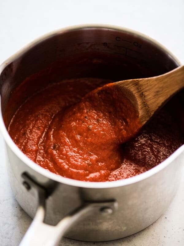 An easy arrabiata sauce in a pot being stirred by a wooden spoon.