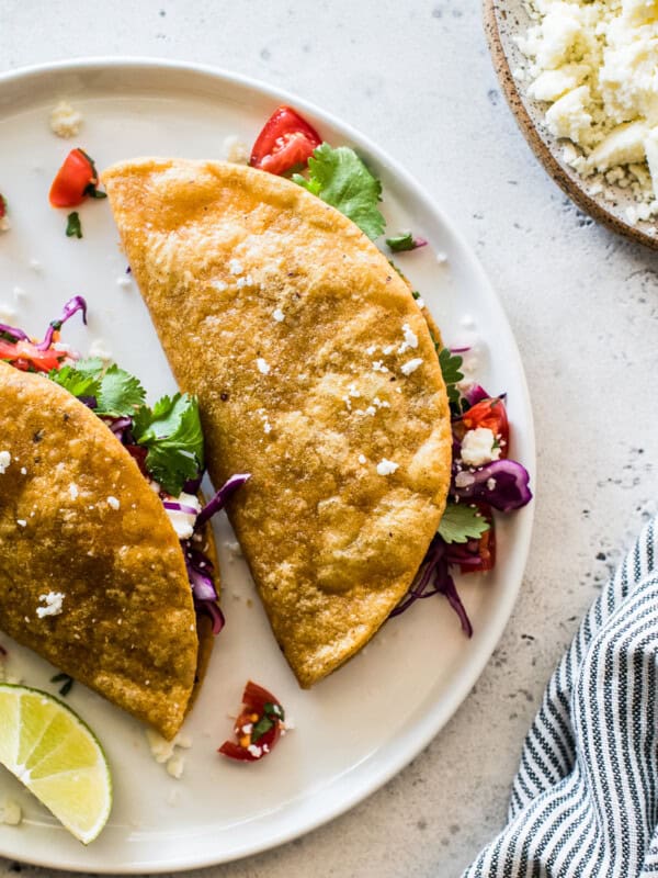 Potato tacos on a white plate stuffed with shredded cabbage and pico de gallo.