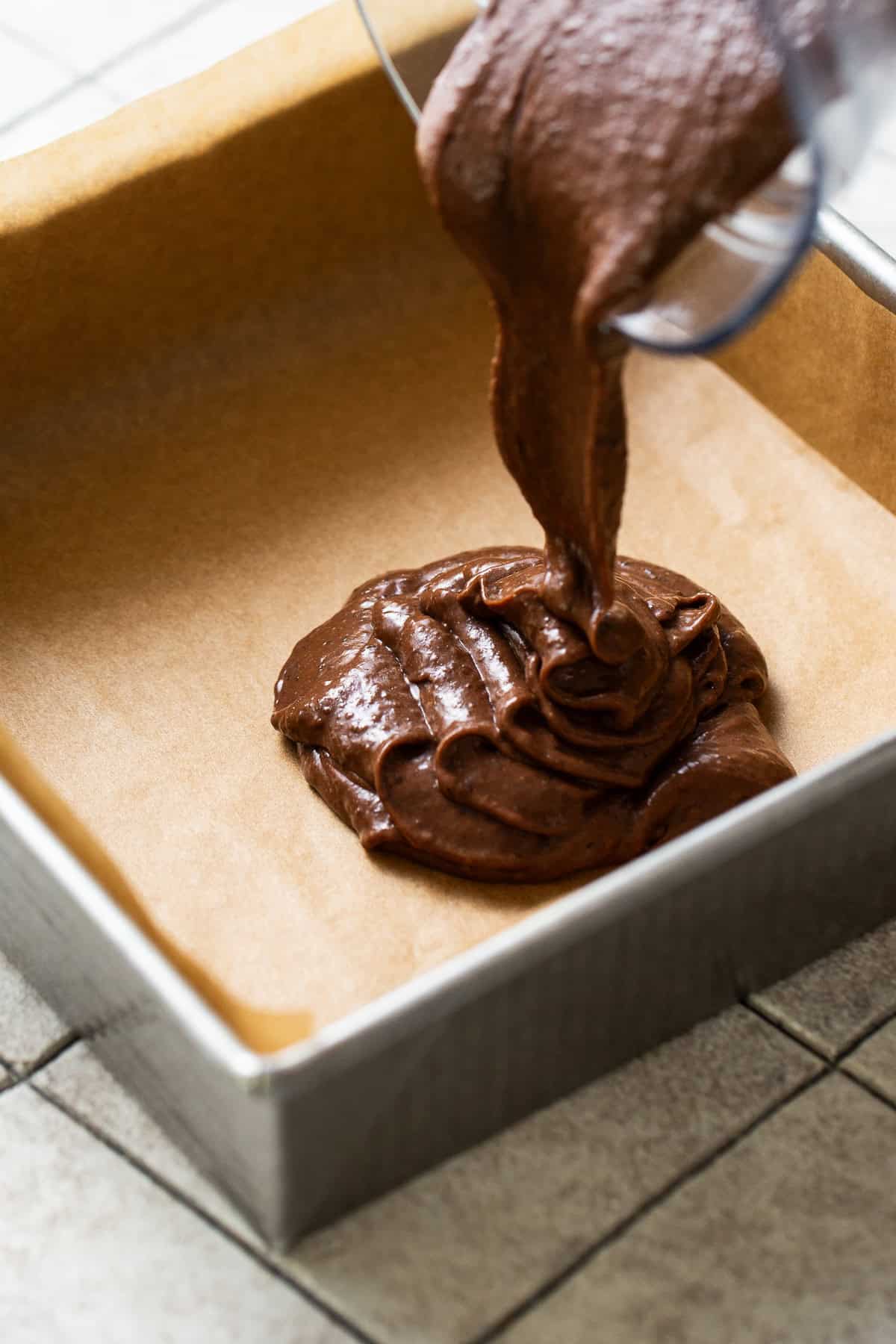 The batter for black bean brownies being poured into a square baking pan lined with parchment paper.