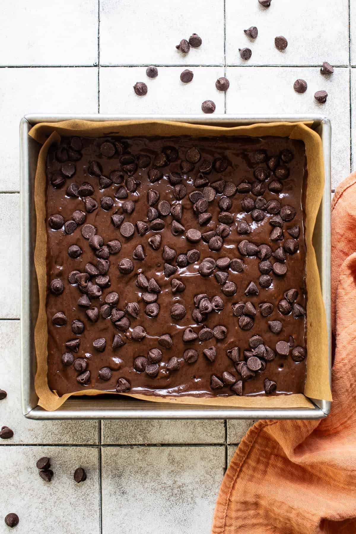 Brownie batter in a square baking pan topped with chocolate chips.