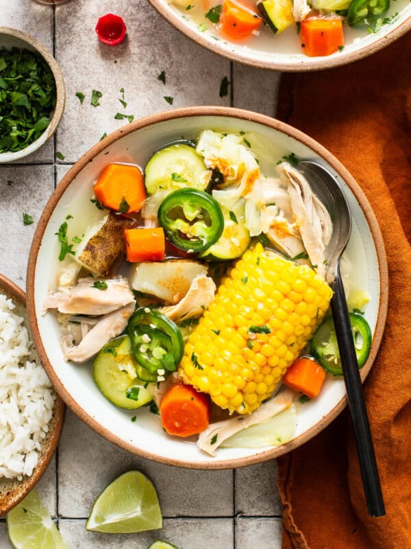 Caldo de pollo (Mexican chicken soup) in a bowl alongside white rice, cilantro, limes, and tabasco.