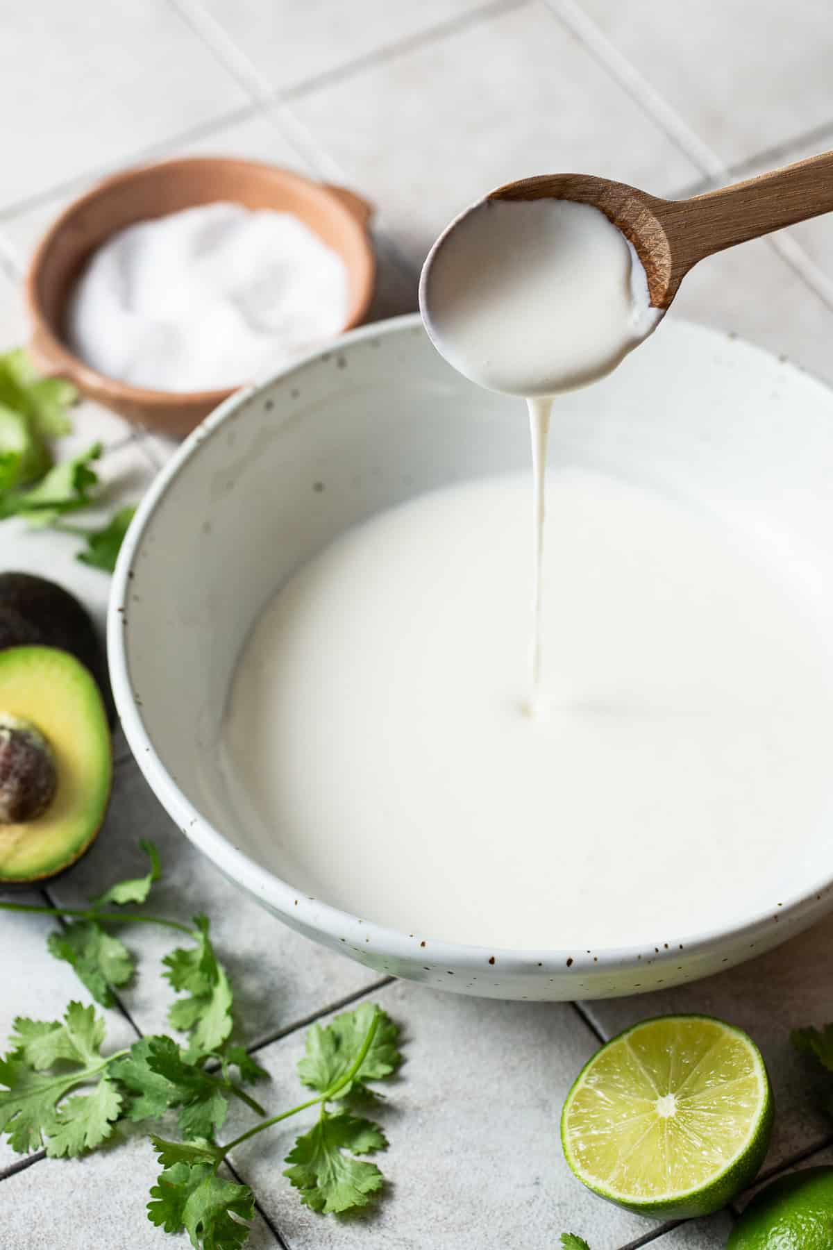 A spoon mixing and pouring some Mexican crema into a bowl.