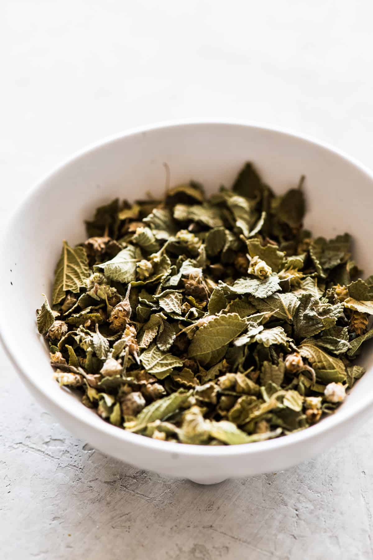 Mexican oregano dried whole leaves in a small white ramekin.