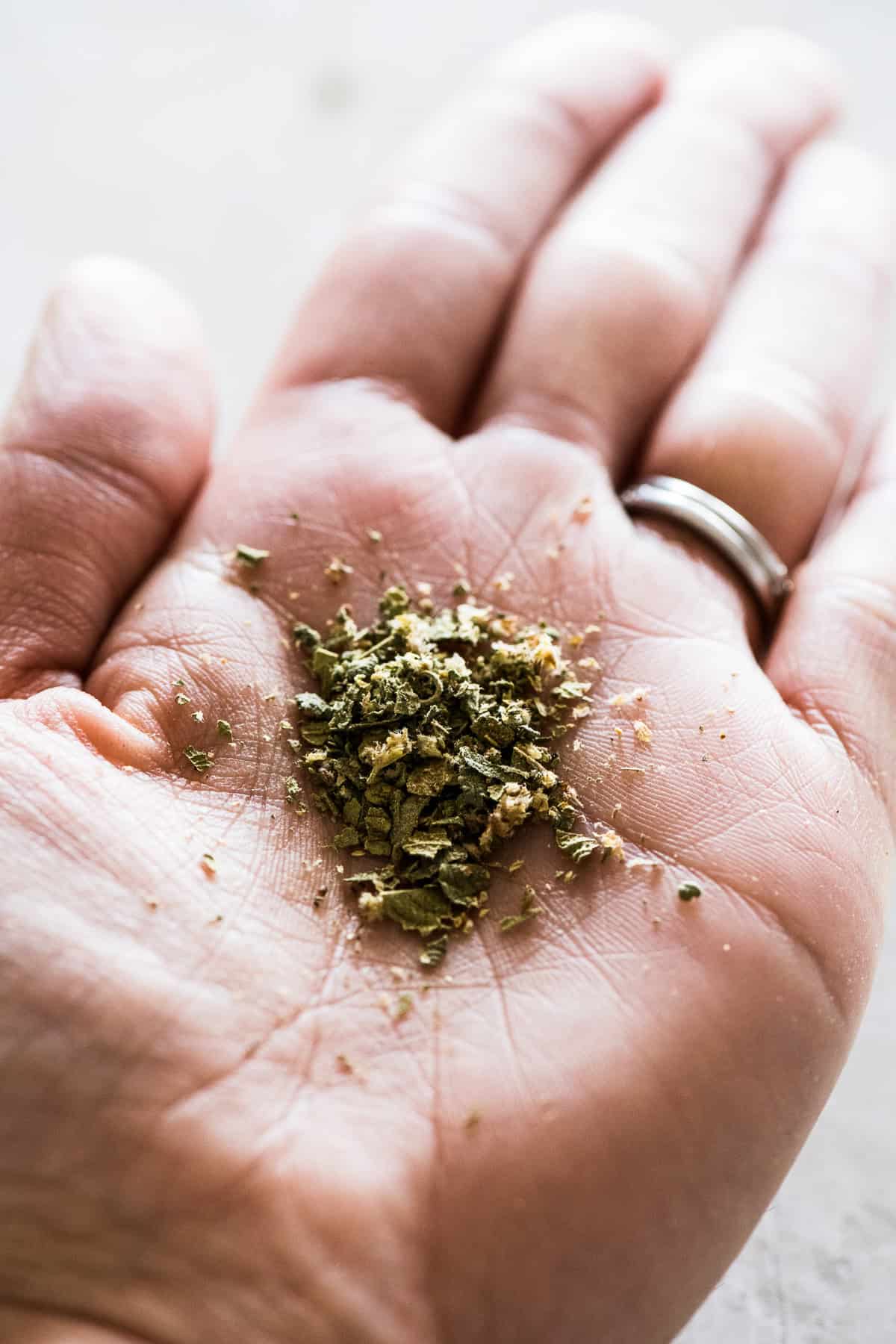 Crushed Mexican oregano in the palm of someone's hand.