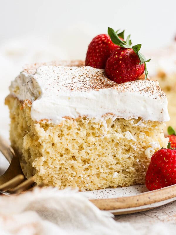 A slice of tres leches cake on a plate topped with whipped cream and fresh strawberries.