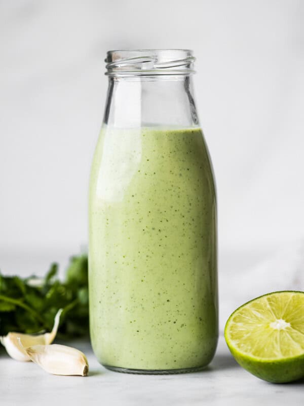 Cilantro Lime Dressing in a jar next to fresh limes and garlic cloves.