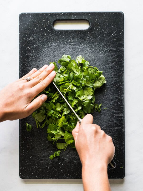 Two hands chopping cilantro on a cutting board.