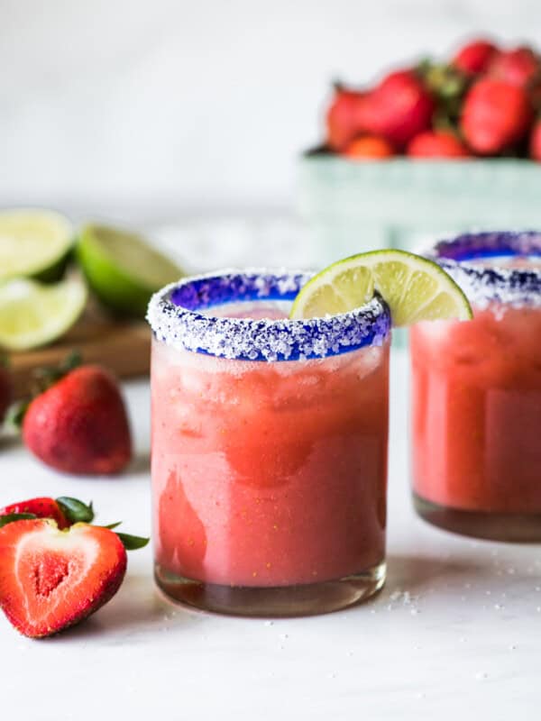 A strawberry margarita in a glass garnished with a lime.