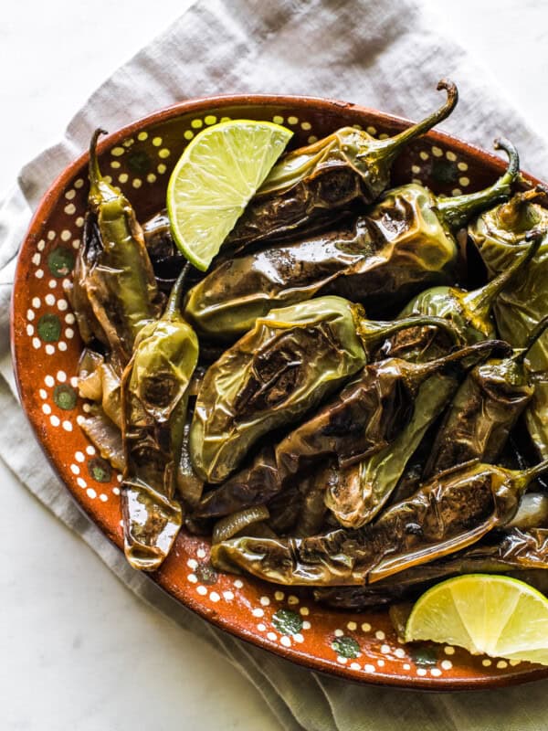 Chiles toreados on a plate with fresh lime wedges.