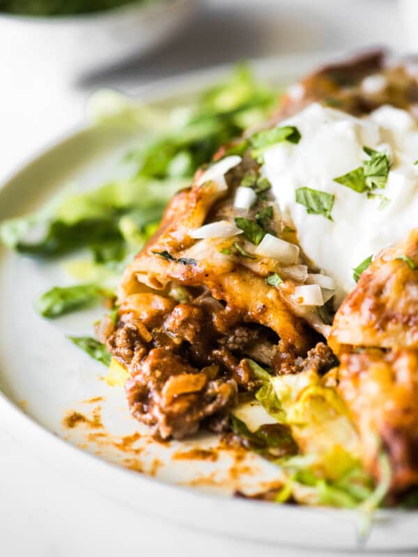 Beef enchiladas topped with sour cream on a bed of shredded lettuce.