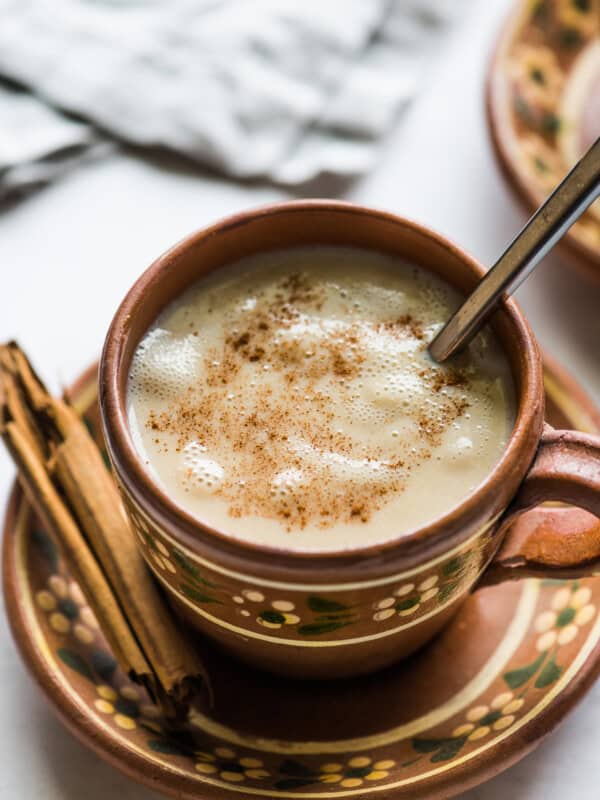 A cup of atole in a Mexican clay mug topped with ground cinnamon.