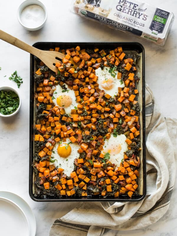 Sheet pan eggs and breakfast hash on a table next to plates.