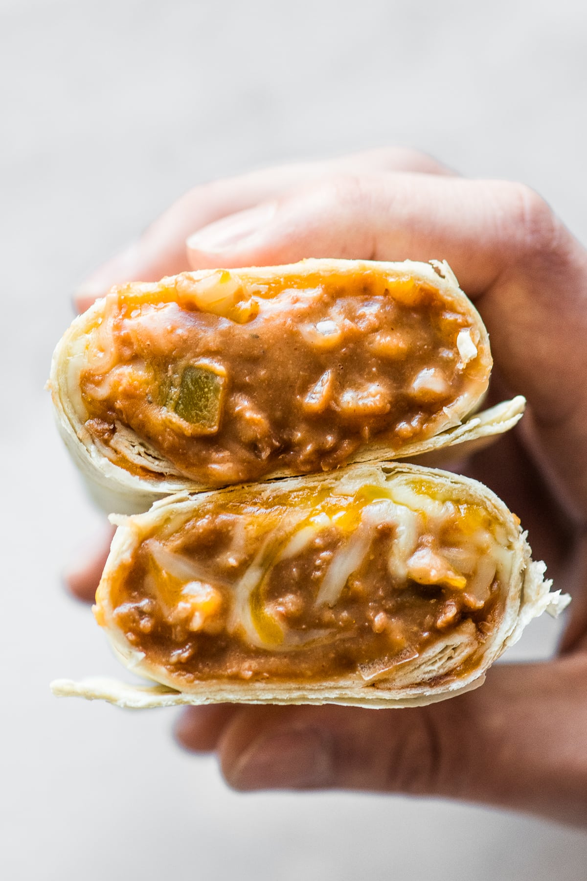 A bean and cheese burrito cut in half with the filling coming out.