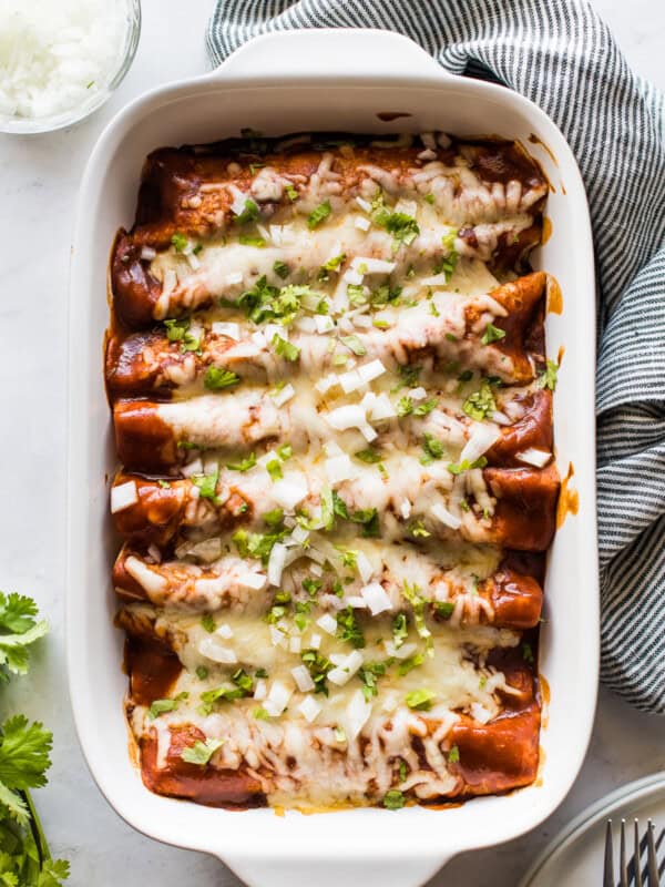 Turkey enchiladas in a baking dish topped with cilantro and onions.