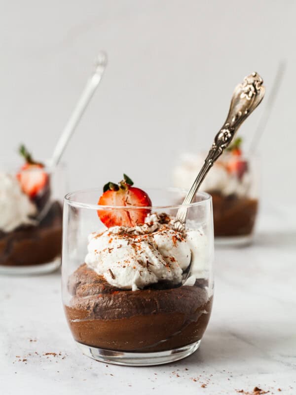 Avocado chocolate mousse in a cup topped with whipped cream and strawberries.