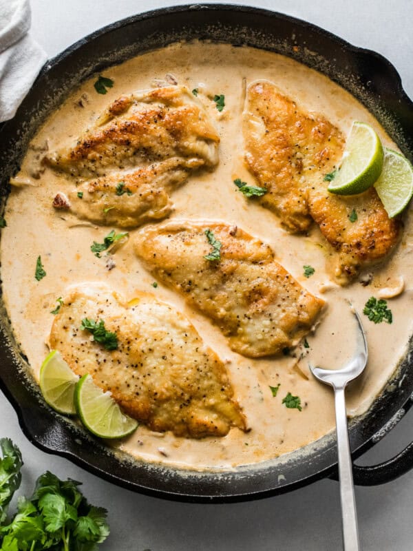 Pollo en Chipotle (Creamy Chipotle Chicken) in a skillet topped with cilantro and lime wedges.