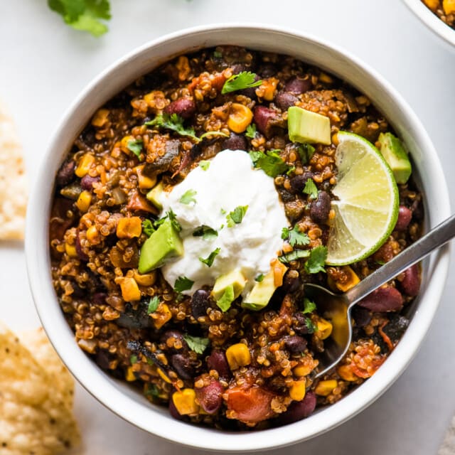 Quinoa black bean chili in a bowl topped with cilantro, avocados, and sour cream.