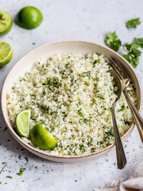 A bowl of cilantro lime cauliflower rice on a table next to fresh limes.