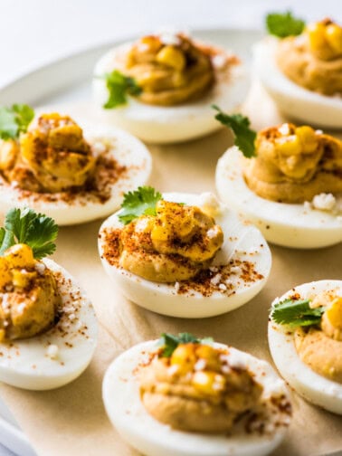 Mexican deviled eggs on a plate topped with corn, cilantro, chili powder, and cotija cheese.