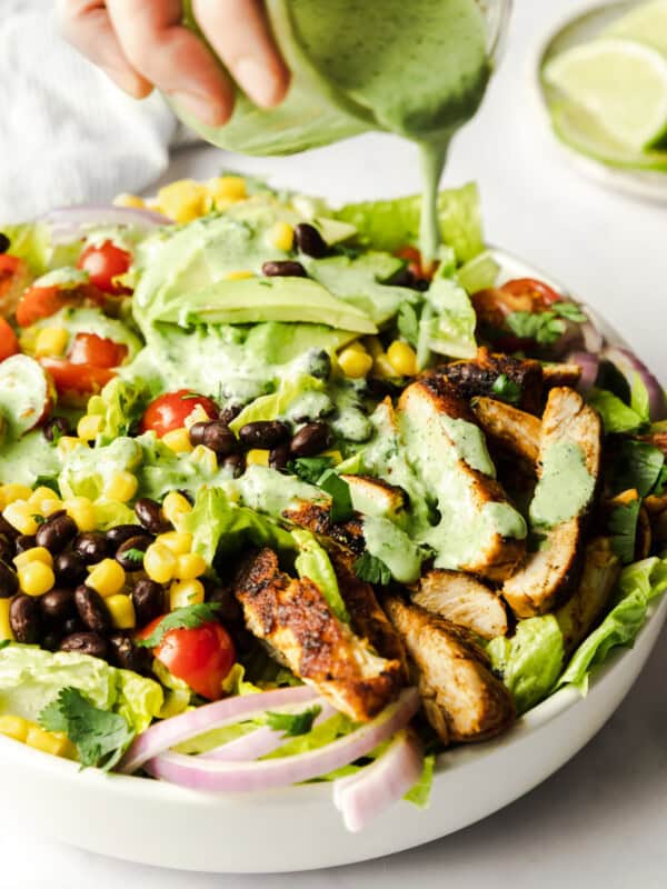 Cilantro-lime dressing being poured on a bowl of southwest chicken salad.