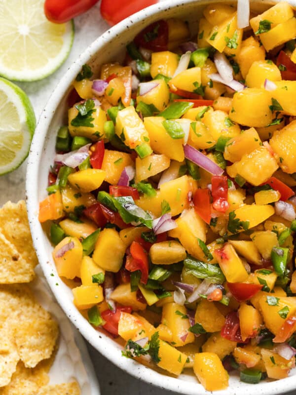 A bowl of peach salsa topped with cilantro and served with tortilla chips.