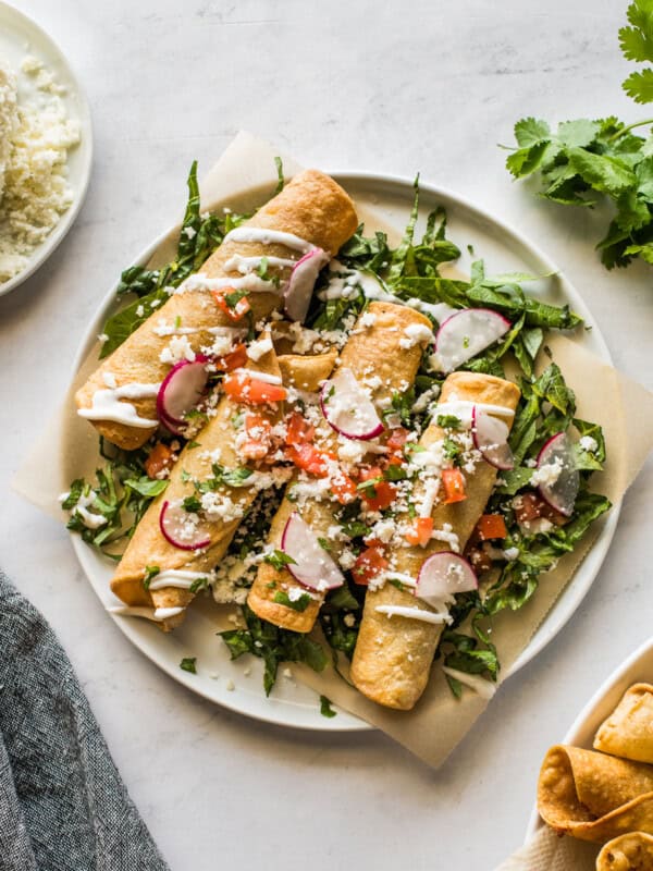 Beef taquitos topped with sour cream, avocado, and tomatoes.