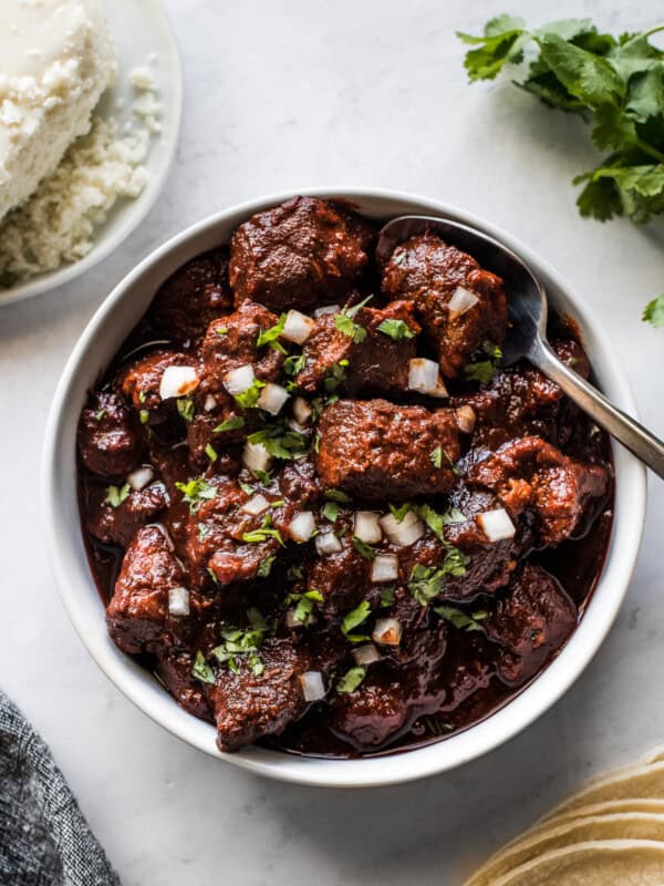 Carne adovada in a bowl next to warm tortillas.