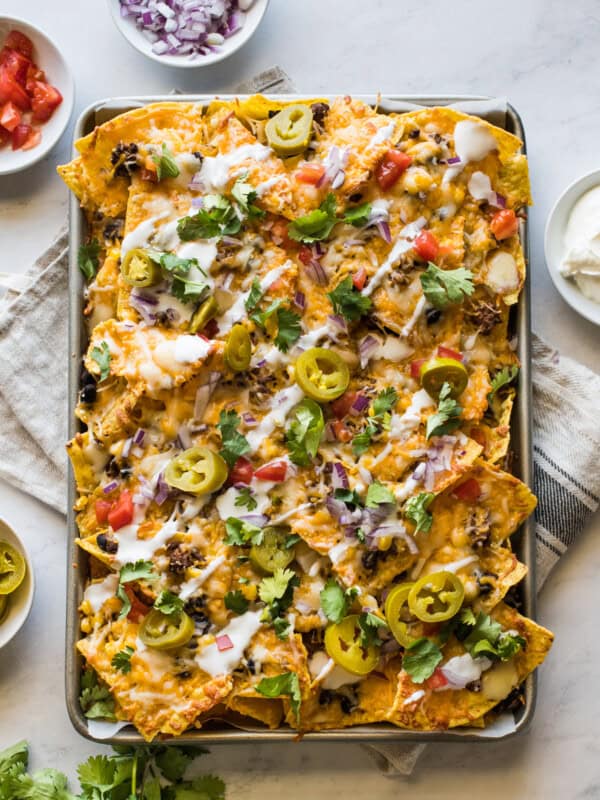 Sheet pan nachos topped with sour cream, pickled jalapenos, tomatoes, and cilantro.