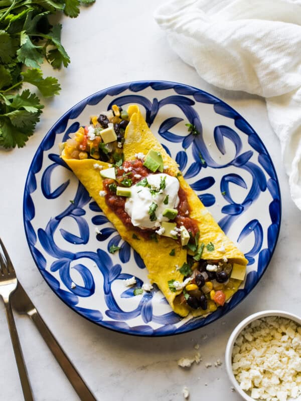 A Mexican omelet on a plate topped with chunky salsa and sour cream.