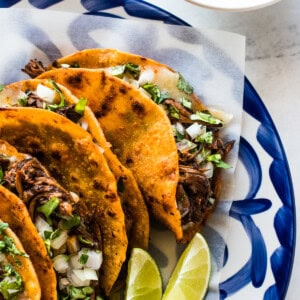 A plate of birria tacos garnished with a lime.