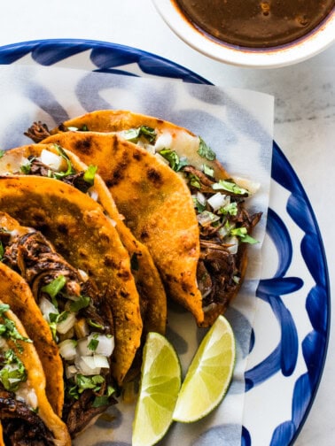 A plate of birria tacos garnished with a lime.