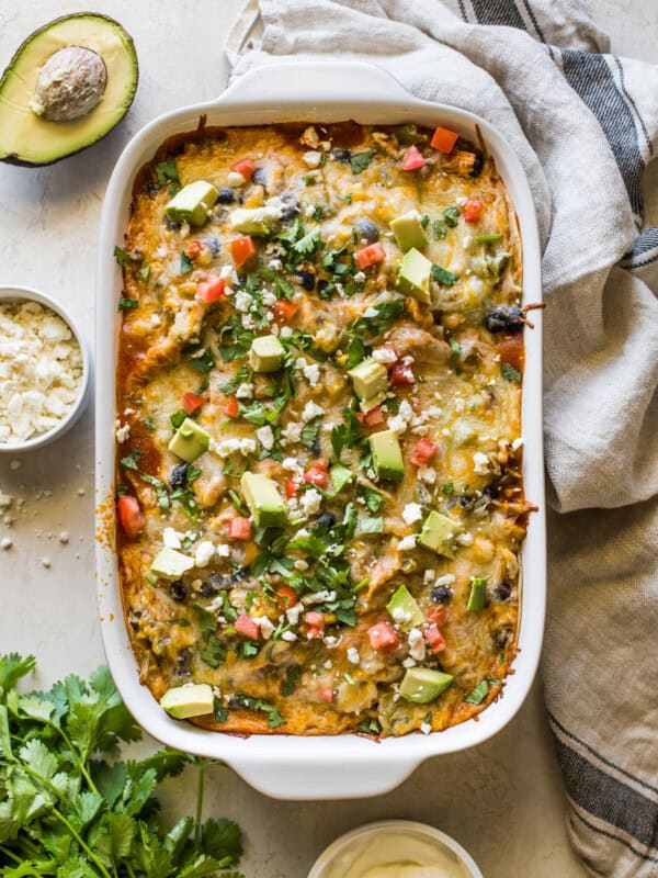 Chicken enchilada casserole topped with cilantro, diced tomatoes, and avocados.