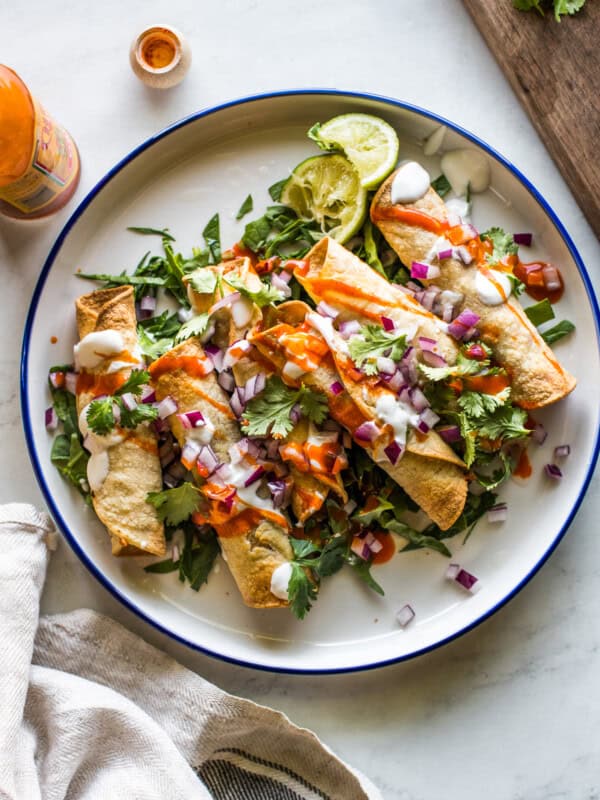 Air fryer chicken taquitos on a plate with lettuce and topped with sour cream, cilantro, salsa, and diced onions.