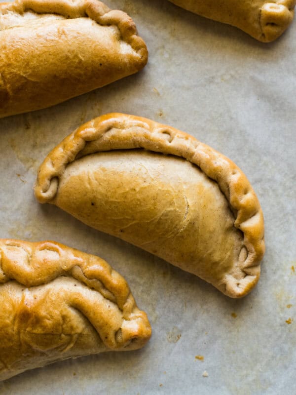 Pumpkin empanadas on a baking tray lined with parchment paper.